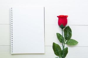 Present gift with red rose flower and notebook on wooden table, 14 February of love day with romantic, copy space with note or diary writing text for you, valentine holiday concept, top view. photo