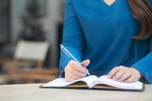 Closeup hand asian woman sitting study and learning writing notebook and diary on table in at cafe shop, girl homework, business writer female working on table, education concept. photo