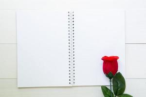 Present red rose flower and notebook with copy space on wooden table, 14 February of love day with romantic, valentine holiday concept, top view. photo