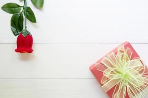 Present gift with red rose flower and gift box with bow ribbon on wooden table, 14 February of love day with romantic, valentine holiday concept, top view. photo