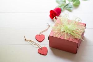 Present gift with red rose flower and gift box with bow ribbon and wood heart shape on wooden table, 14 February of love day with romantic, valentine holiday concept. photo