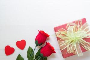 Present gift with red rose flower and gift box with bow ribbon and heart on wooden table, 14 February of love day with romantic, valentine holiday concept, top view.