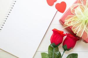 presente flor de rosa roja y cuaderno y caja de regalo y forma de corazón con espacio de copia en la mesa de madera, 14 de febrero del día del amor con el concepto romántico de vacaciones de San Valentín. foto