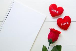 Presente flor de rosa roja y cuaderno y forma de corazón con espacio de copia en mesa de madera, 14 de febrero del día del amor con concepto romántico de vacaciones de San Valentín, vista superior. foto