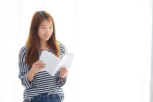 Beautiful of portrait young asian woman relax standing reading book on bedroom at home, girl study literature, education and lifestyle concept. photo