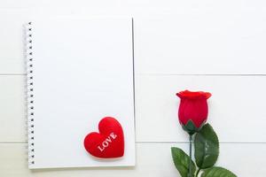 Present red rose flower and notebook and heart shape with copy space on wooden table, 14 February of love day with romantic, valentine holiday concept. photo