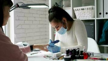 Female manicurist in a face mask making a manicure in the salon. Master servising her client. Nails care procedure.
