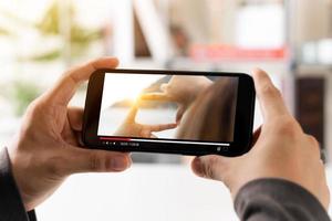 Online movie streaming with smartphone. Young man watching a movie on a mobile phone with an imaginary video player service. photo