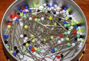 Close up view on lots of sewing pins with colored heads in a metal box on a wooden table photo