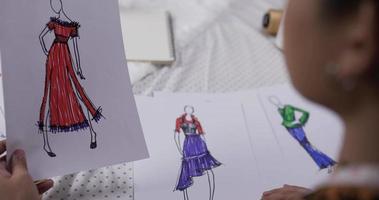 Cierra la mano del diseñador de moda revisando un papel de ropa de boceto en el estudio. el pequeño empresario de inicio está en proceso de crear una nueva colección de ropa. video