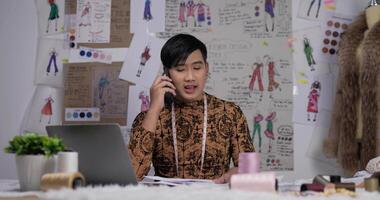 Portrait of Angry Asian clothing designer man talking on mobile phone in the studio. Startup small businessman is in process of creating a new clothes collection. video