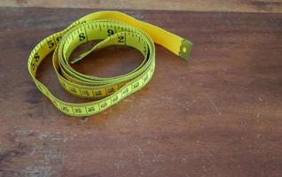 Sewing concept. Yellow tape measure isolated on a brown wooden background. photo