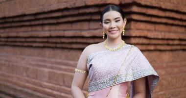 porträtt av thailändsk kvinna i traditionell kostym tittar på kameran och ler i antika tempel. video