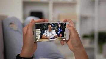Nahaufnahme einer Frau, die zu Hause ein Smartphone anschaut. asiatischer lehrer mann im kopfhörer streamt live-video auf dem bildschirm mobil mit viel emoji wie und emotion liebe. Fernlernkonzept.
