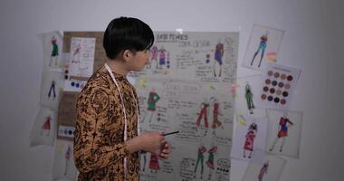 Portrait of Asian clothing designer man working in the studio. Startup small businessman is in process of creating a new clothes collection. video