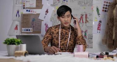 retrato de un diseñador de ropa asiático enojado hablando por teléfono móvil en el estudio. el pequeño empresario de inicio está en proceso de crear una nueva colección de ropa.