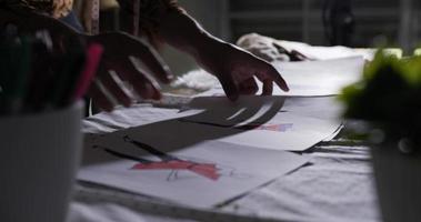 close-up do estilista masculino asiático verificando dados em papel ou contemplando desenhos à noite. designer de roupas de homem focado trabalhando em seu escritório. video