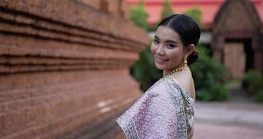 retrato de una mujer tailandesa con traje tradicional mirando a la cámara y caminando en un templo antiguo. video