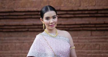 retrato de mujer tailandesa saludo de respeto en traje tradicional de tailandia. mujer joven mirando a la cámara y sonriendo en el antiguo templo. video