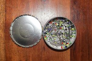 Close up view on lots of sewing pins with colored heads in a metal box on a wooden table photo