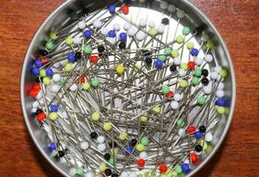 Close up view on lots of sewing pins with colored heads in a metal box on a wooden table photo