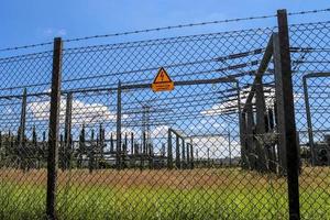 Sign showing the words high voltage in german language at the fence of a big substation distributing electric energy with lots power lines on a sunny day photo