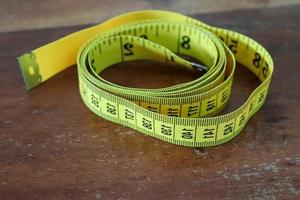 Sewing concept. Yellow tape measure isolated on a brown wooden background. photo