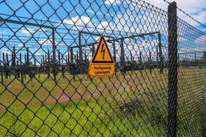 Sign showing the words high voltage in german language at the fence of a big substation distributing electric energy with lots power lines on a sunny day photo