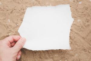 concepto mano sosteniendo un papel blanco en blanco sobre un fondo de arena marrón, papel en blanco para su carta. foto