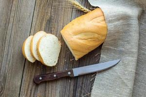 Sliced bread with wheat spikes on wooden table closeup photo