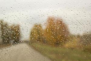 The car rides along the autumn road with rain drops on the windshield car window photo