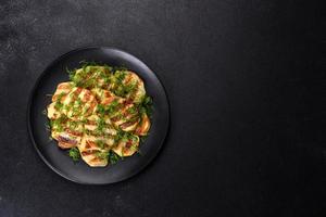 Delicious grilled potato slices with spices and herbs on a black plate photo