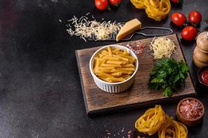 Raw tagliatelle paste with grated cheese, cherry tomatoes, spices and herbs on a wooden cutting board