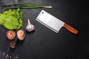 An axe for meat, spices and herbs, a cutting board against a dark concrete background