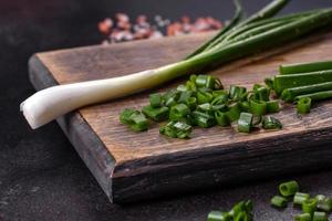 Fresh green onions on a cutting board. Dark concrete background photo