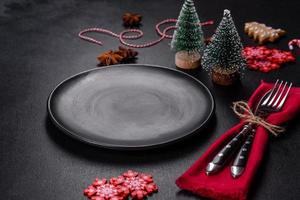 Christmas table setting with empty black ceramic plate, fir tree and black accessories photo