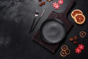Christmas table setting with empty black ceramic plate, fir tree and black accessories photo