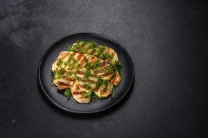 Delicious grilled potato slices with spices and herbs on a black plate photo