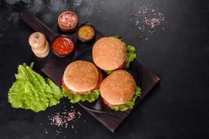 tres hamburguesas con hamburguesa de carne de res y verduras frescas sobre fondo oscuro foto
