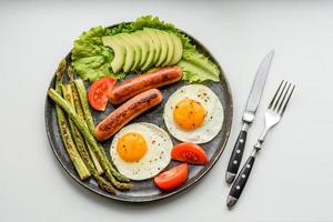 A delicious nourishing breakfast with fried eggs, sausages, asparagus, tomatoes, avocado, spices and herbs photo