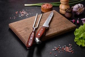 Fork, knife, spices and herbs, cutting board on a dark concrete background photo