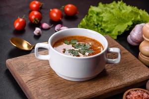Fresh delicious tomato soup with spices and parsley in a white bowl on a wooden board photo