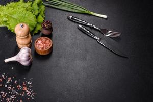 Fork, knife, spices and herbs, cutting board on a dark concrete background photo