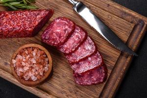 salami ahumado con romero, ajo y tomates en tabla de cortar de madera foto