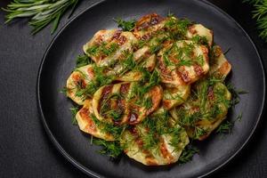 Delicious grilled potato slices with spices and herbs on a black plate photo