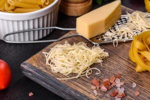 Raw tagliatelle paste with grated cheese, cherry tomatoes, spices and herbs on a wooden cutting board photo