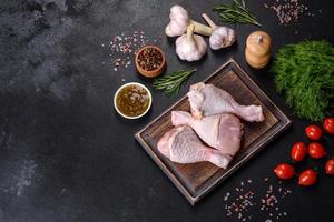 tres piernas de pollo crudo con especias y hierbas en una tabla de cortar de madera foto