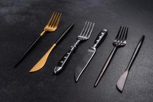 Several knives and forks in black gold and silver on a dark concrete background photo