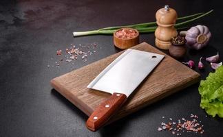 An axe for meat, spices and herbs, a cutting board against a dark concrete background photo