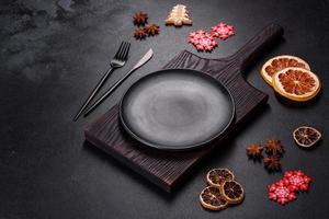Christmas table setting with empty black ceramic plate, fir tree and black accessories photo